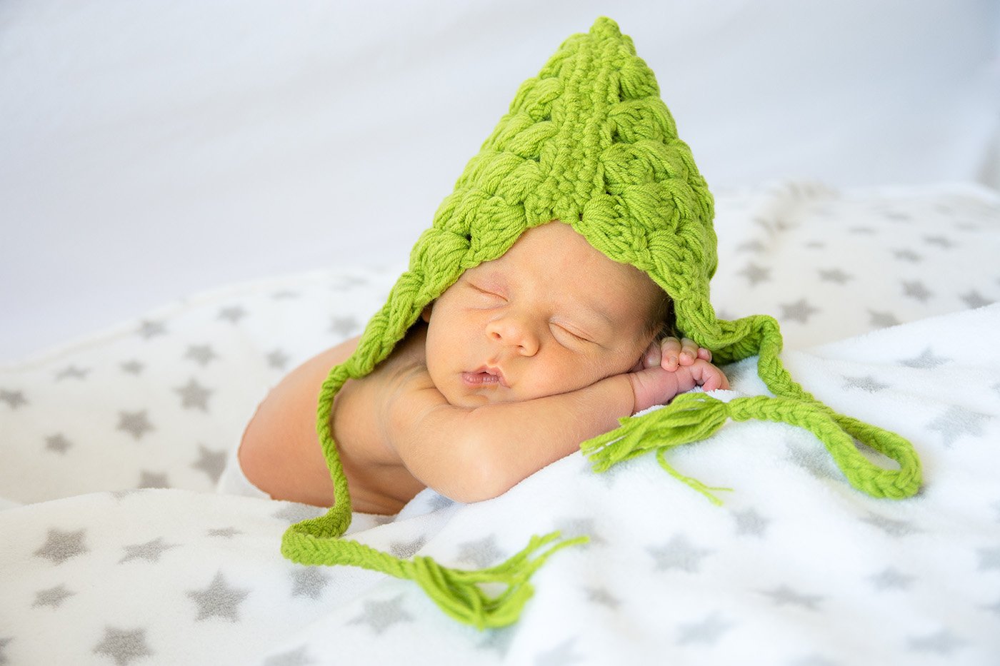 Photo de naissance, bébé avec un bonnet vert dans un drap blanc
